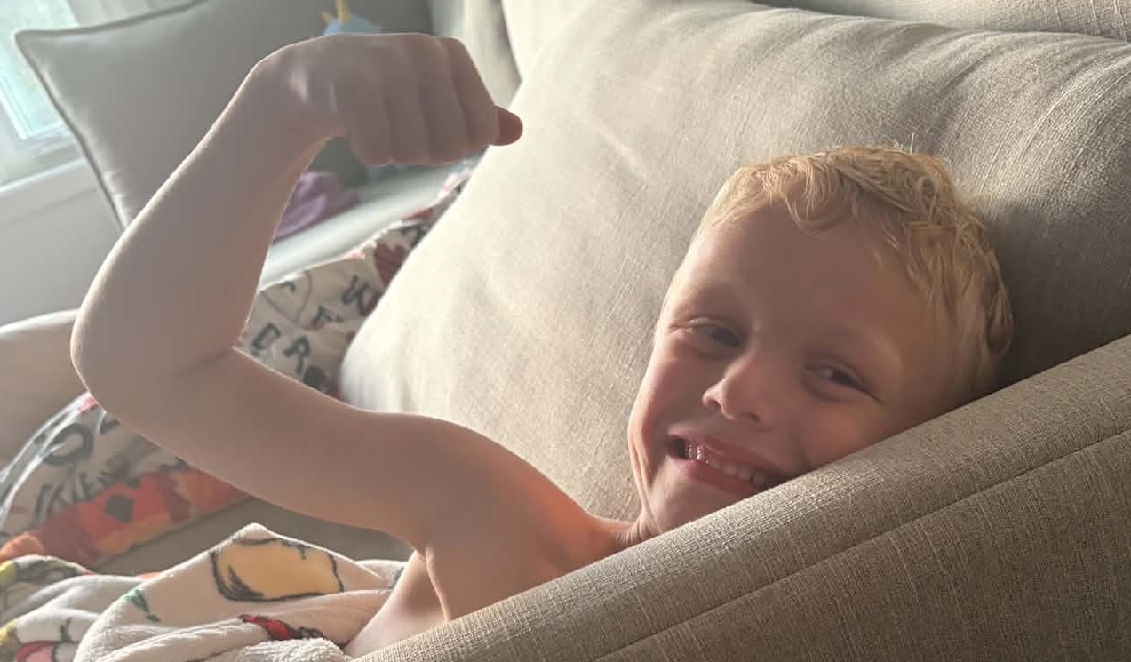 A smiling little boy flexing his arm at storytime — Real food, real STRONG!